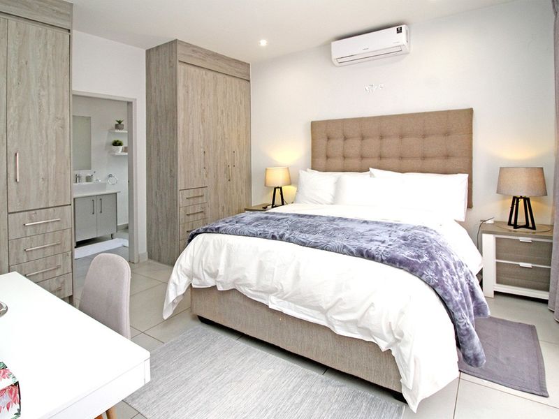 A well-maintained bedroom featuring built-in cupboards, tiled flooring, an air conditioning unit, and direct access to an en-suite bathroom.