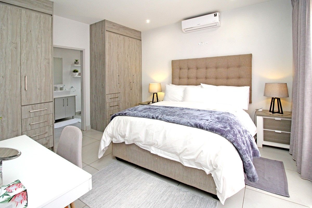 A well-maintained bedroom featuring built-in cupboards, tiled flooring, an air conditioning unit, and direct access to an en-suite bathroom.