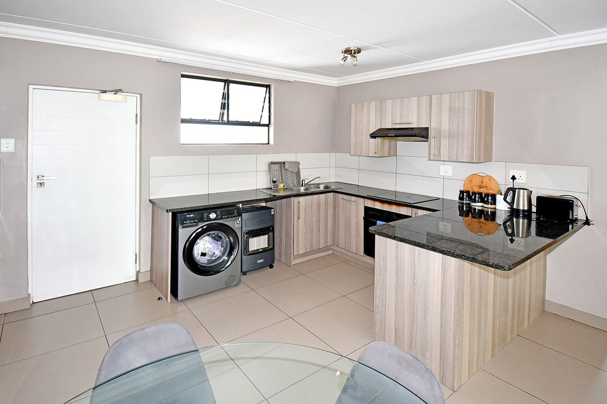 Modern kitchen featuring light wood-grain cabinetry, granite countertops, built-in oven, extractor fan, and tiled flooring with a functional layout.