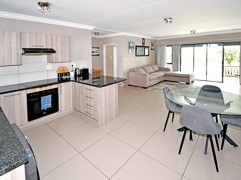 Spacious open-plan living area featuring a modern kitchen with granite countertops, built-in appliances, and tiled flooring, flowing seamlessly to a bright lounge and patio access.
