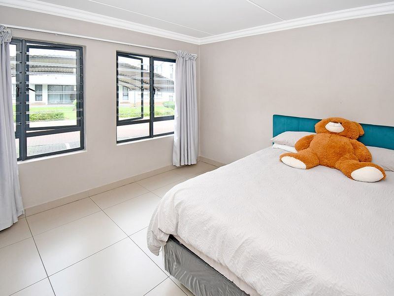 A bright bedroom featuring neutral tiled flooring, crown molding, and large aluminium-framed louvered windows providing natural light.