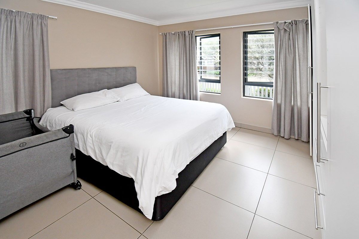 A well-maintained bedroom featuring neutral tiled flooring, built-in cupboards, and louvered windows that provide natural light.
