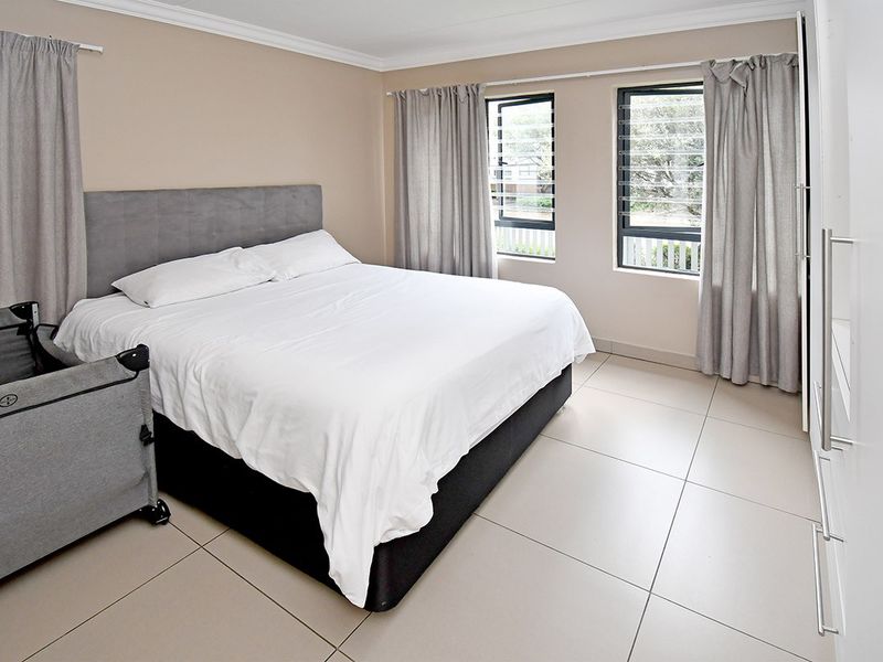 A well-maintained bedroom featuring neutral tiled flooring, built-in cupboards, and louvered windows that provide natural light.