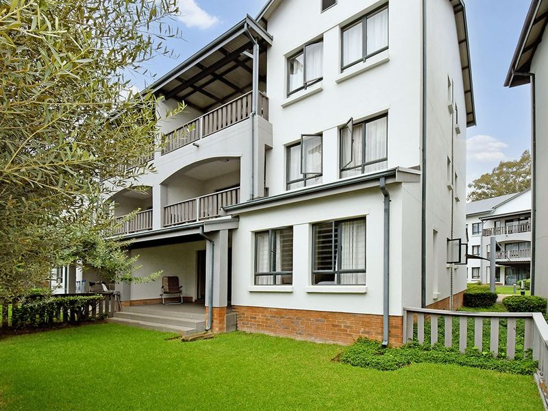 Rear view of a multi-story apartment building featuring balconies, brick base detailing, and a well-maintained lawn area.