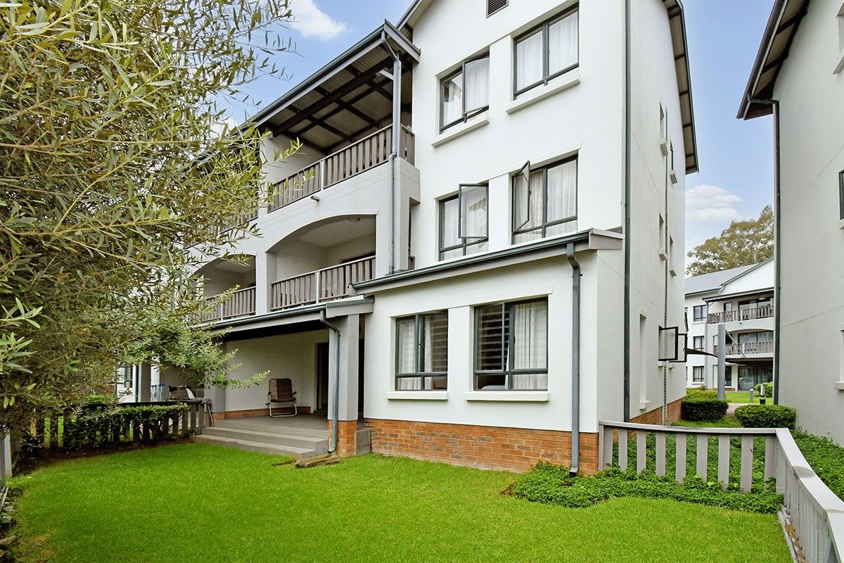 Rear view of a multi-story apartment building featuring balconies, brick base detailing, and a well-maintained lawn area.