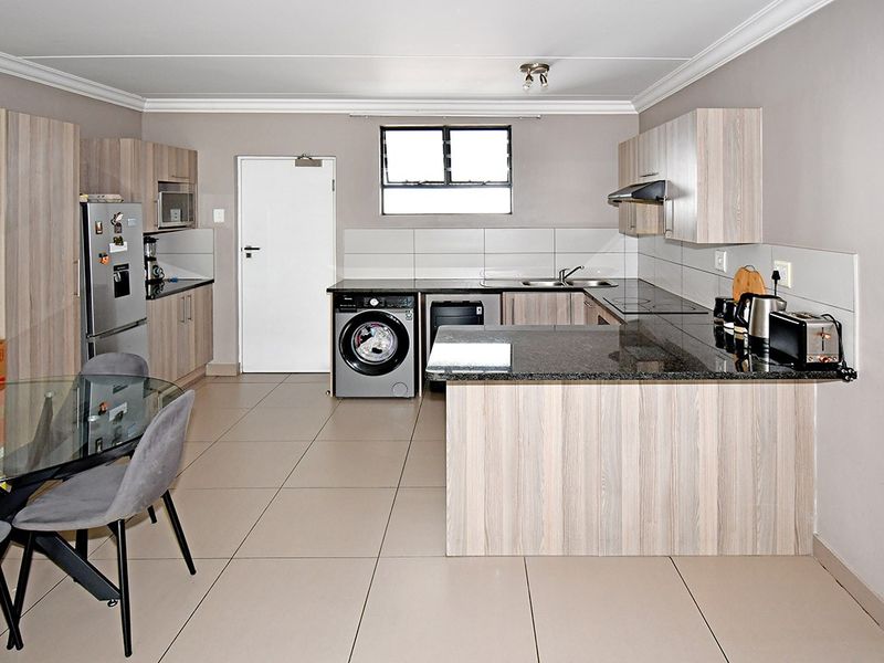 Modern open-plan kitchen featuring light wood-grain cabinetry, granite countertops, integrated appliances, and neutral tiled flooring, creating a functional and cohesive living space.