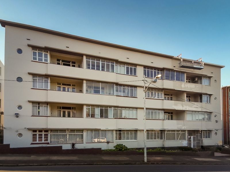 Front elevation of a multi-story apartment building featuring balconies, casement windows, and security grilles, showing signs of exterior paint wear.