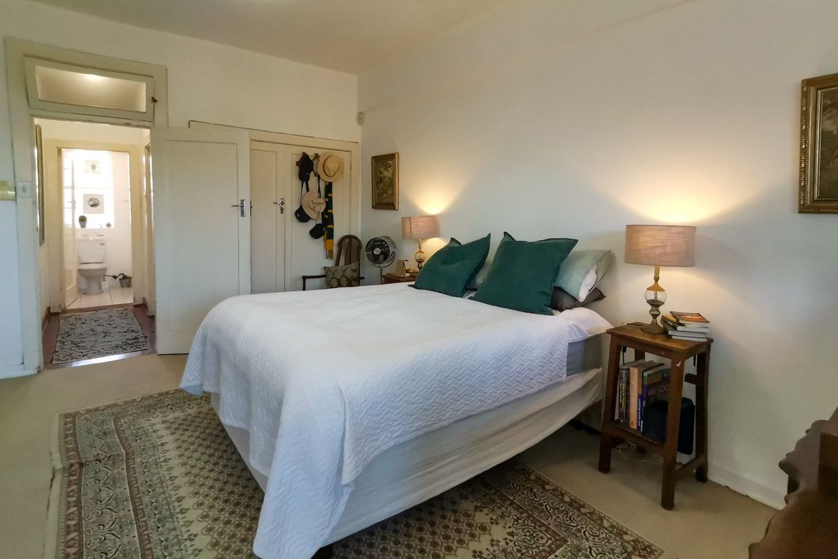 A well-lit bedroom featuring built-in cupboards and a transom window, with an adjoining view into a bathroom area.