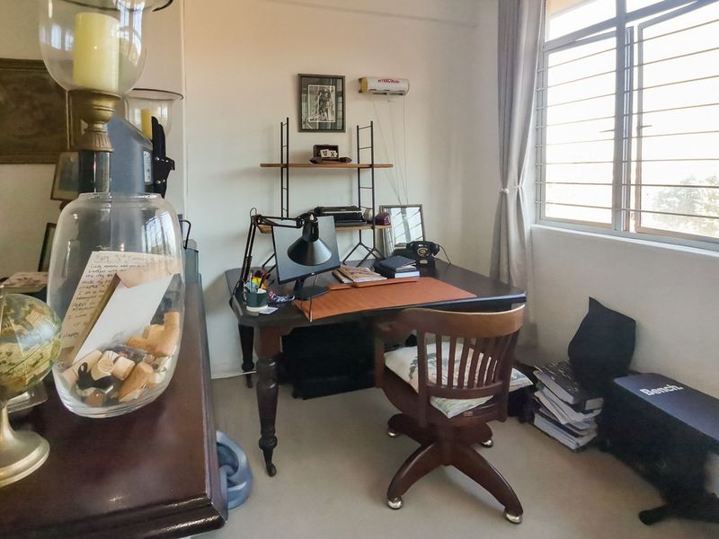 A functional home office space featuring a large window with security bars and a wall-mounted air conditioning unit.