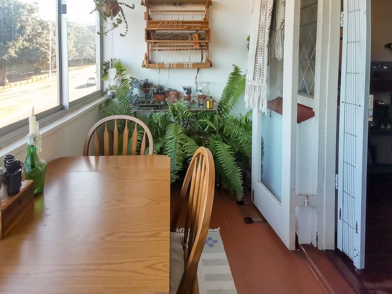 A sunlit enclosed balcony or sunroom featuring timber flooring, large sliding windows, and access through classic french doors.