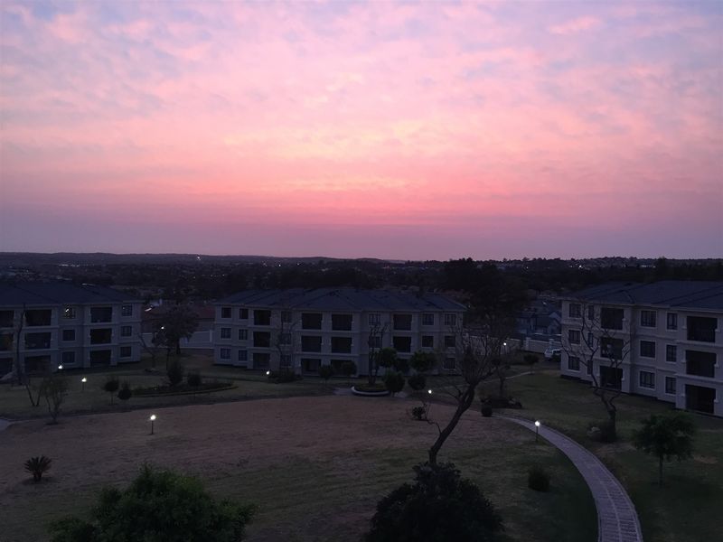Elevated sunset view overlooking the apartment complex grounds, featuring manicured lawns, paved walkways, and exterior building facades.