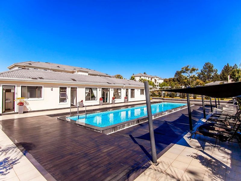 A well-maintained outdoor pool area featuring a rectangular swimming pool, timber decking, and a shade sail structure set against the apartment building exterior.