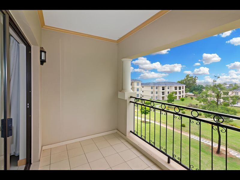 A clean, covered balcony featuring tiled flooring, a decorative column, and a wrought iron balustrade, offering pleasant views of the surrounding estate grounds.