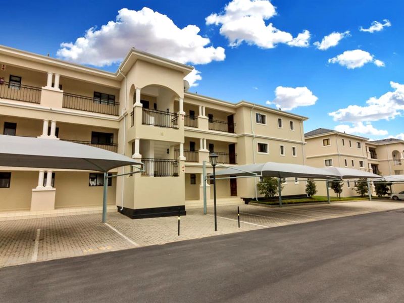 Exterior view of a multi-story apartment complex featuring paved parking areas with shade cloth carports and private balconies with wrought iron railings.