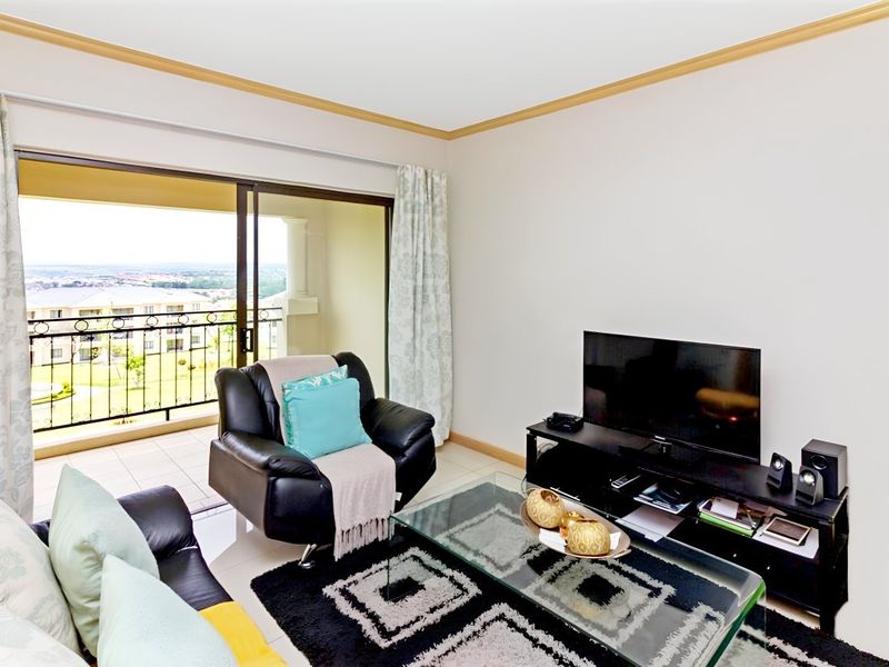A living room featuring tiled floors, coving, and a large sliding glass door providing access to a balcony with scenic views.