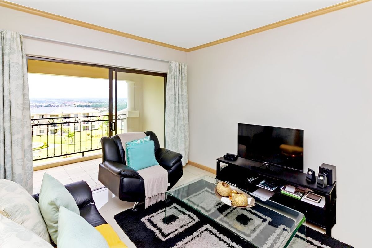 A living room featuring tiled floors, coving, and a large sliding glass door providing access to a balcony with scenic views.