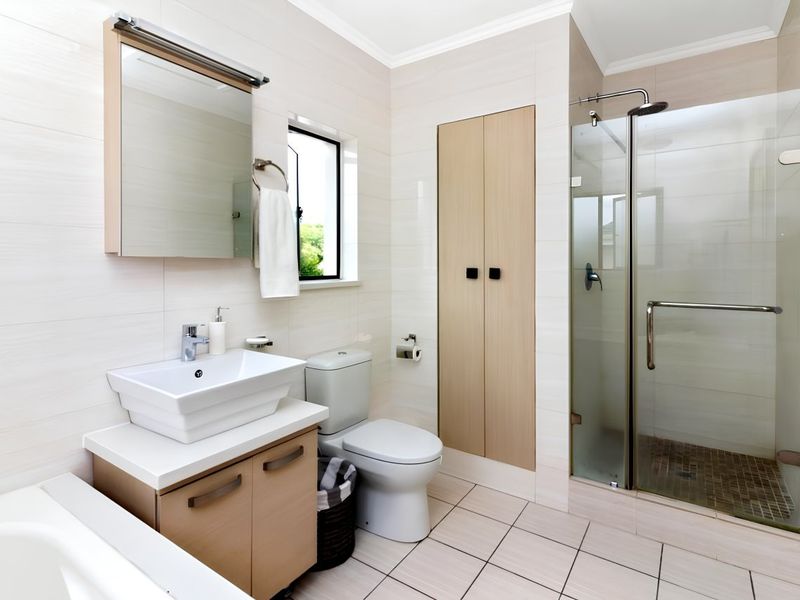 Modern bathroom featuring a vessel sink vanity, built-in storage cupboard, toilet, and a glass-enclosed shower with neutral wall and floor tiling.
