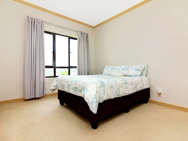 A simple bedroom featuring neutral carpeted flooring, light-toned walls, and an aluminium-framed window with curtains.