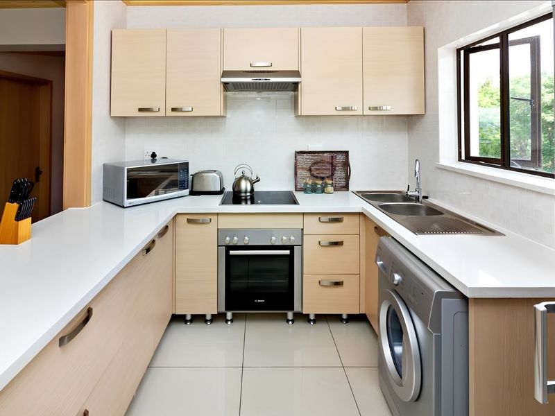 Modern kitchen featuring light wood cabinetry, stone countertops, integrated oven and hob, and tiled flooring with a functional layout.