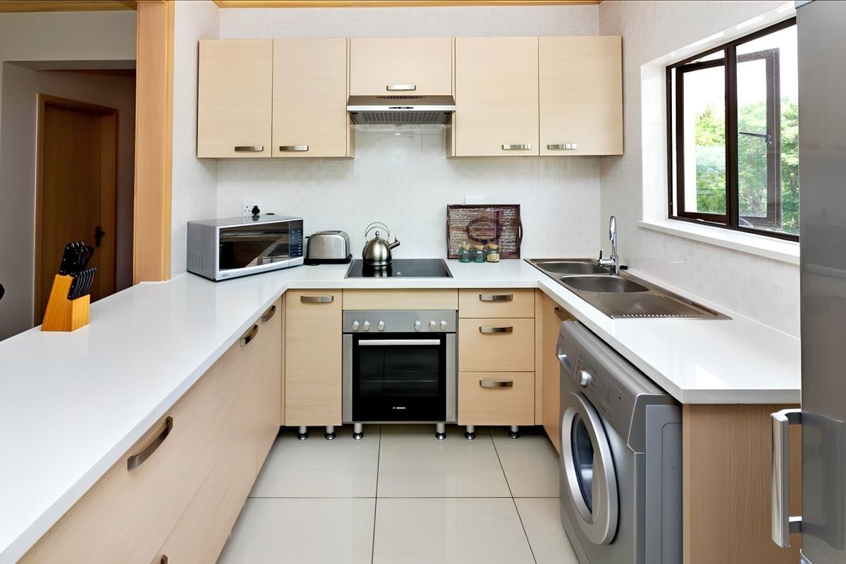 Modern kitchen featuring light wood cabinetry, stone countertops, integrated oven and hob, and tiled flooring with a functional layout.