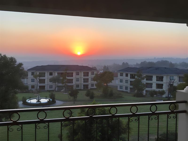 Scenic sunset view overlooking a well-maintained communal garden with a central water fountain, framed by a decorative wrought iron balcony railing.