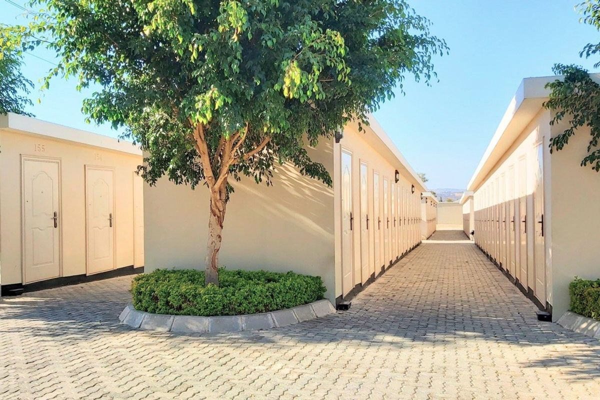 A well-maintained exterior corridor featuring paved walkways, multiple unit access doors, and landscaped garden areas between the apartment blocks.