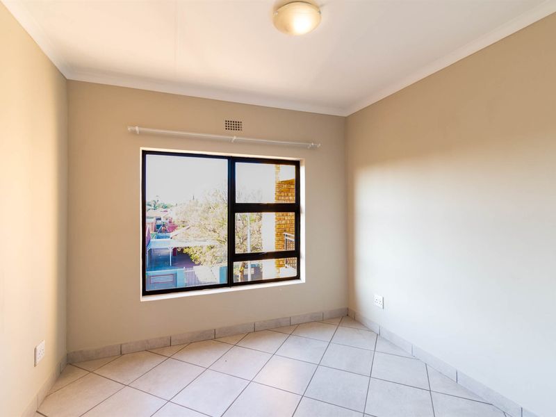 A bright, empty bedroom featuring neutral wall tones, tiled flooring, and a large aluminium-framed window providing natural light.