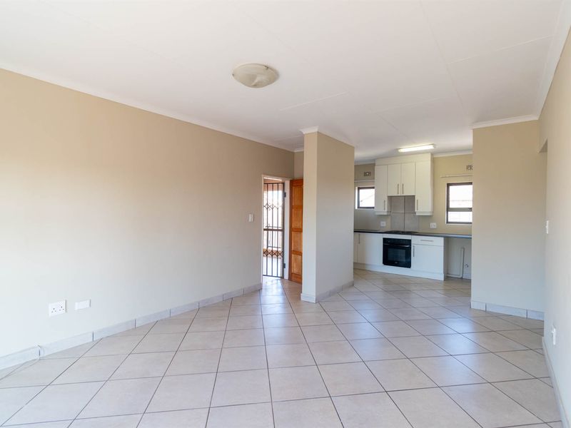 An open-plan living and kitchen area featuring neutral tiled flooring, built-in cabinetry, and an integrated oven, offering a clean and functional layout.