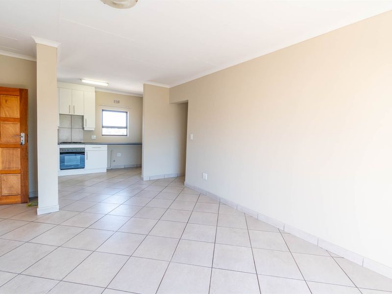 An open-plan living and kitchen area featuring neutral tiled flooring, built-in cabinetry, and a functional kitchen layout with integrated appliances.
