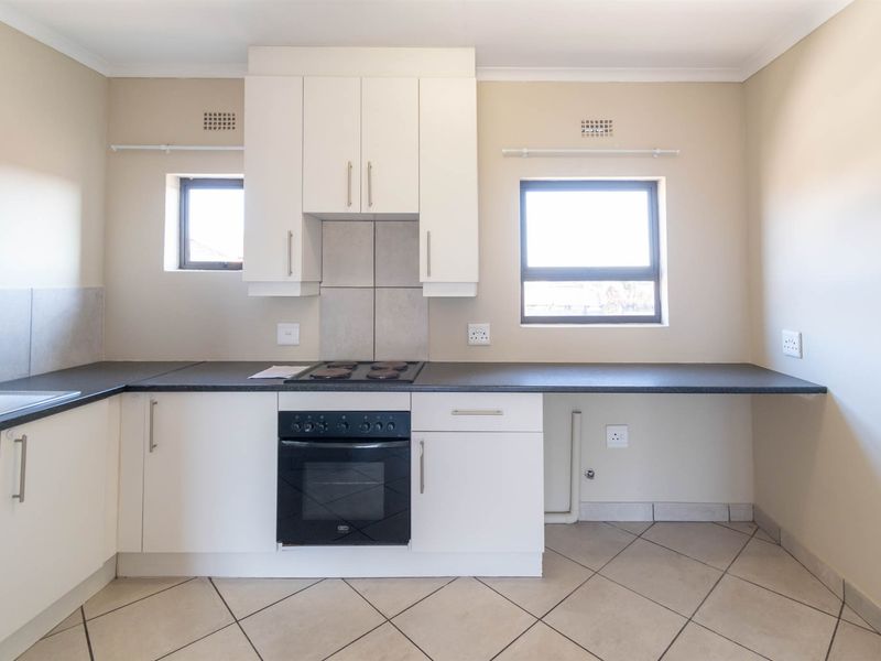 A clean, functional kitchen featuring white cabinetry, dark laminate countertops, built-in oven and hob, and neutral tiled flooring.
