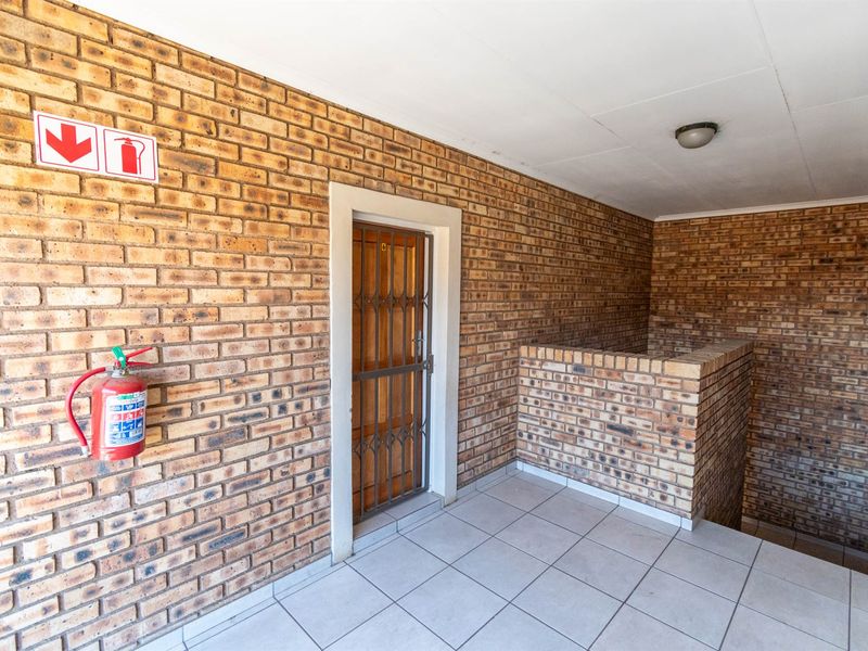 A functional apartment entrance area featuring face brick walls, tiled flooring, and a secure metal gate.