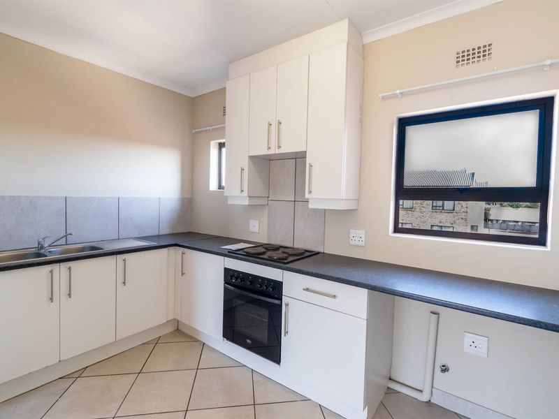 A clean, functional kitchen featuring white cabinetry, dark laminate countertops, built-in oven and hob, tiled backsplash, and neutral tiled flooring.