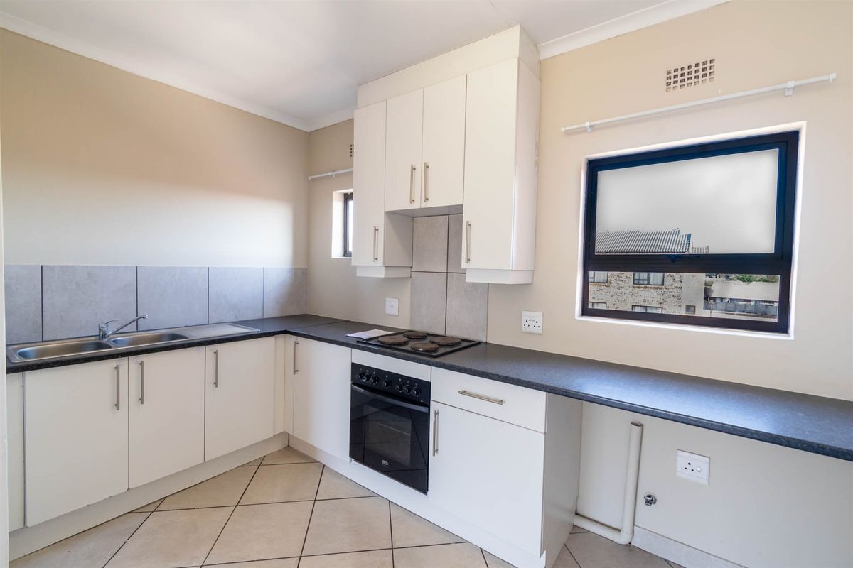 A clean, functional kitchen featuring white cabinetry, dark laminate countertops, built-in oven and hob, tiled backsplash, and neutral tiled flooring.