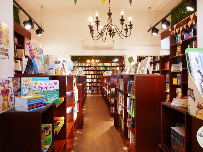 A well-maintained retail bookstore interior featuring extensive built-in wooden shelving, track lighting, and a central chandelier.