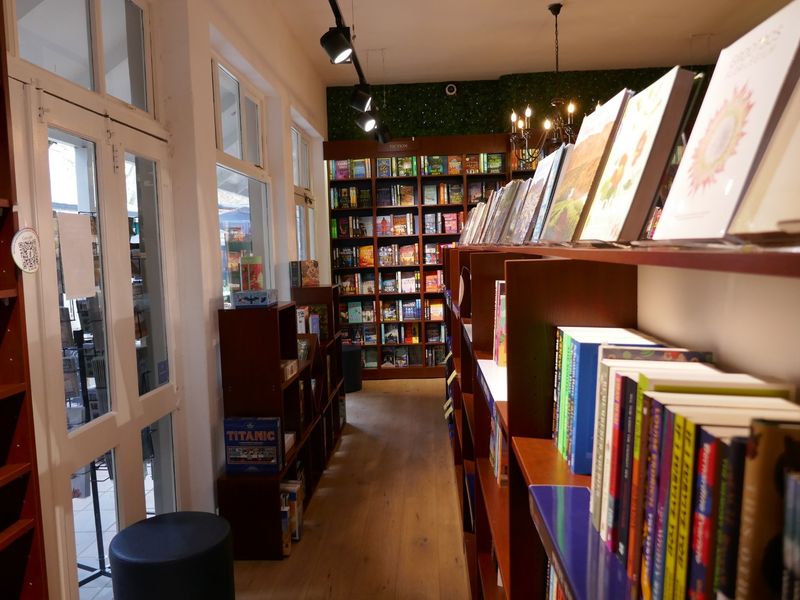 A well-maintained retail bookstore interior featuring extensive built-in wooden shelving, track lighting, and a decorative artificial green wall.