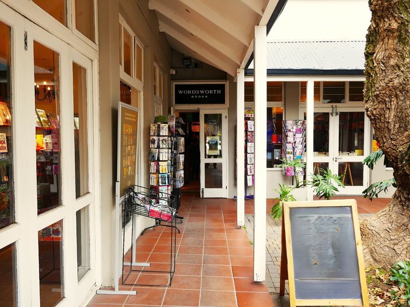 A covered outdoor walkway featuring tiled flooring and glass-fronted retail entrances, providing a welcoming pedestrian access point for the commercial property.