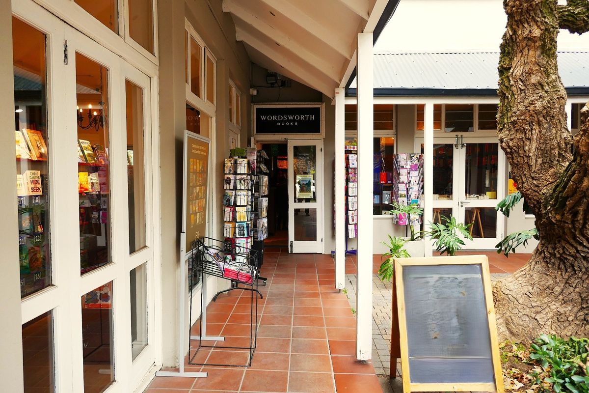 A covered outdoor walkway featuring tiled flooring and glass-fronted retail entrances, providing a welcoming pedestrian access point for the commercial property.