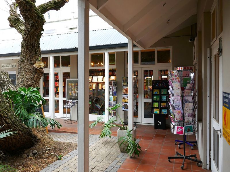 A covered outdoor walkway featuring terracotta tiling and timber support posts, providing access to retail storefronts with glass-paneled doors.