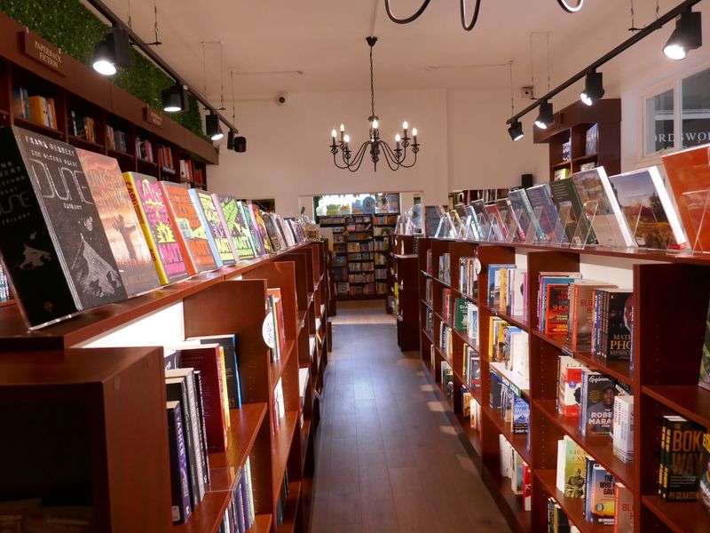 A well-maintained retail bookstore interior featuring extensive built-in wooden shelving, modern track lighting, and a central chandelier.