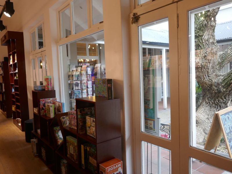 Interior view of a retail space featuring built-in wooden shelving, track lighting, timber flooring, and large glass windows looking out onto a courtyard.