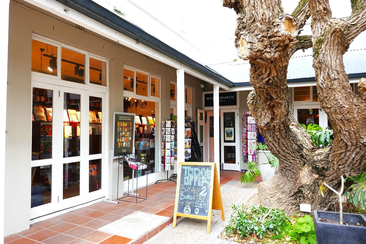 A charming retail storefront featuring a covered tiled walkway, large glass display windows, and a welcoming entrance area with mature landscaping.