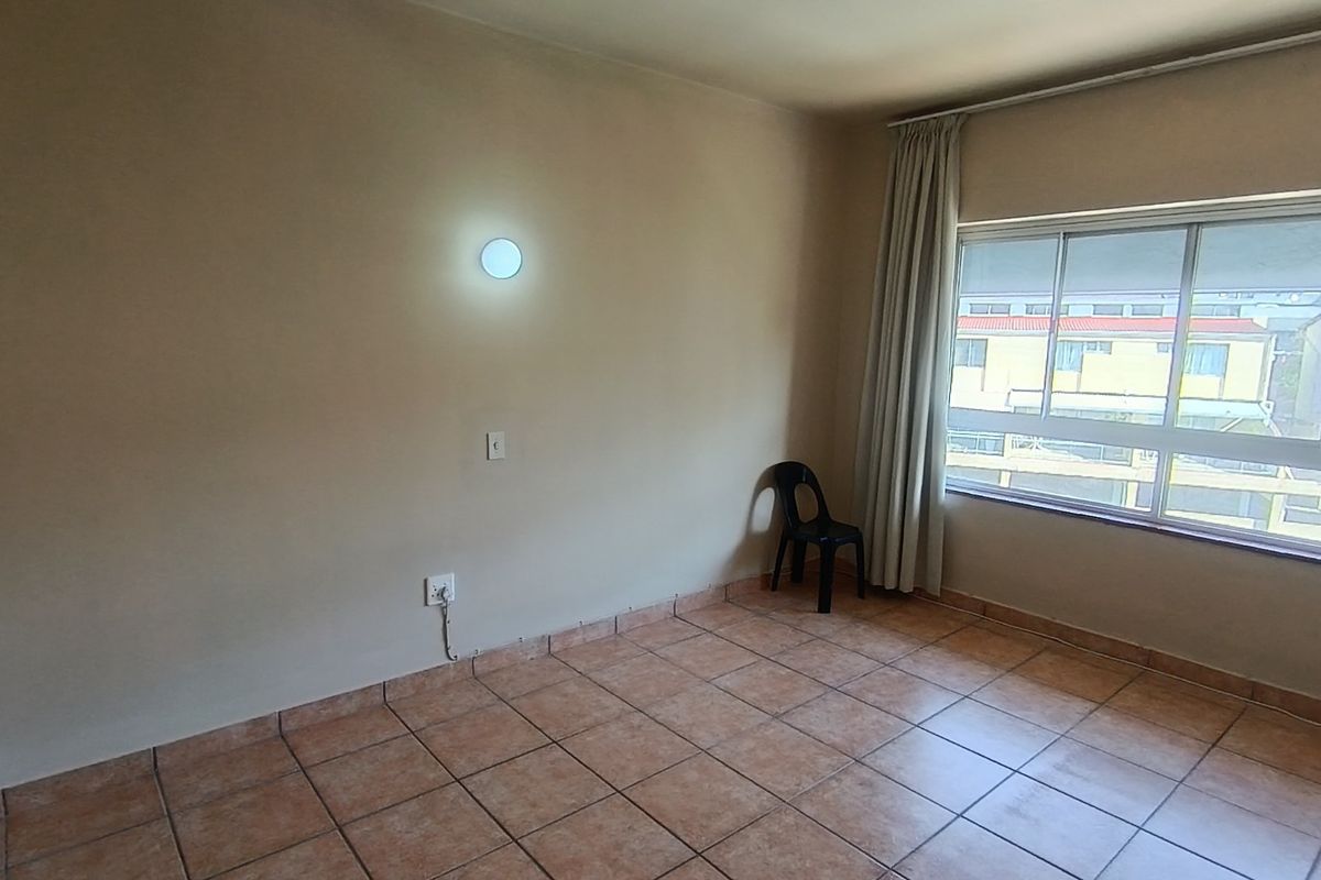 A vacant bedroom featuring neutral tiled flooring, a large sliding window with curtain tracks, and a wall-mounted light fixture.