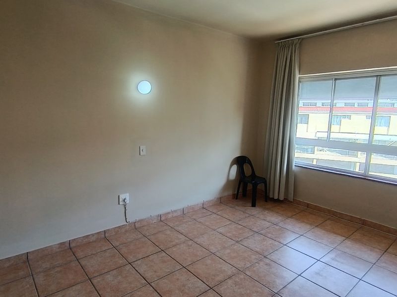 A vacant bedroom featuring neutral tiled flooring, a large sliding window with curtain tracks, and a wall-mounted light fixture.
