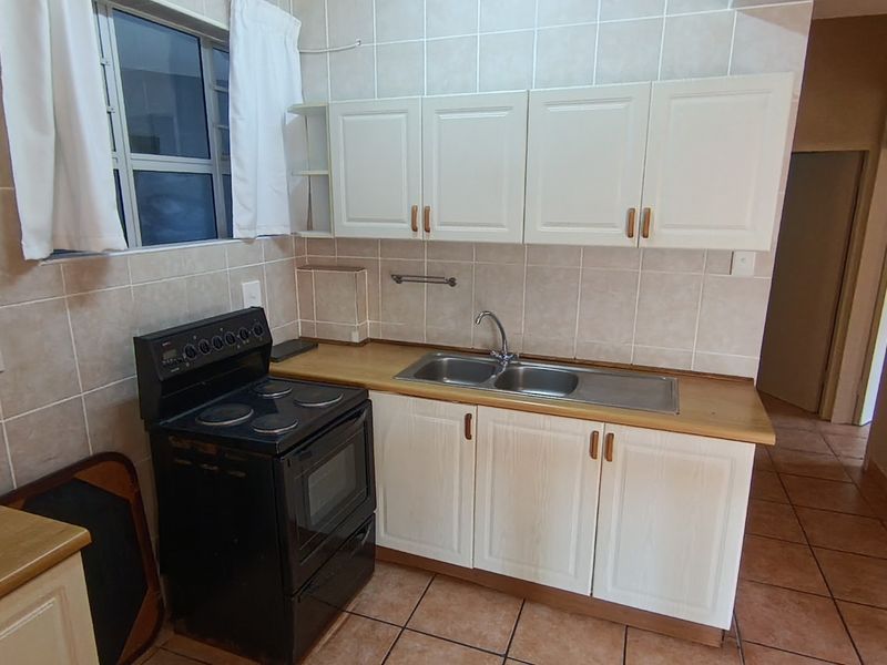 A functional kitchen featuring white cabinetry, a double basin sink, tiled backsplash, and tiled flooring, providing a clean and practical workspace.