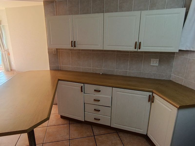A functional kitchen area featuring built-in cabinetry, laminate countertops, a breakfast bar, and tiled finishes, offering a clean and practical layout.