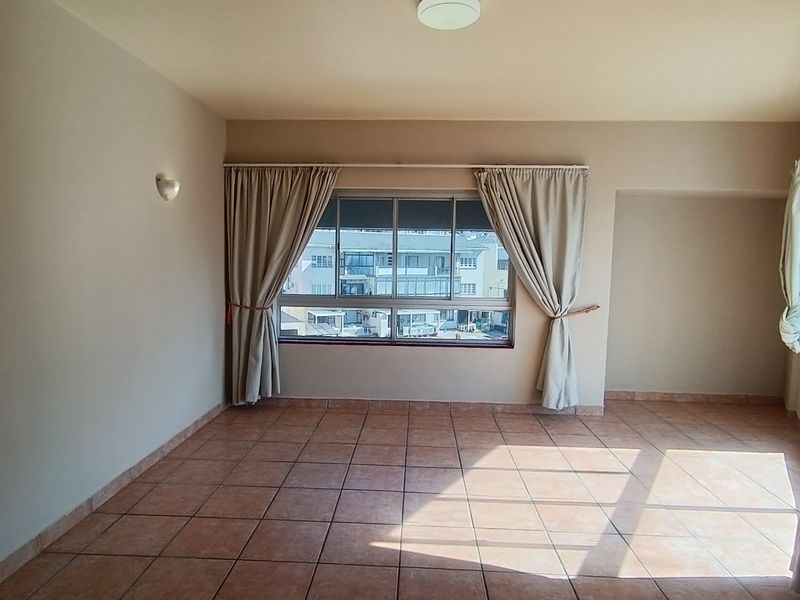 A spacious, empty living area featuring neutral walls, tiled flooring, and large windows that provide natural light and an urban outlook.