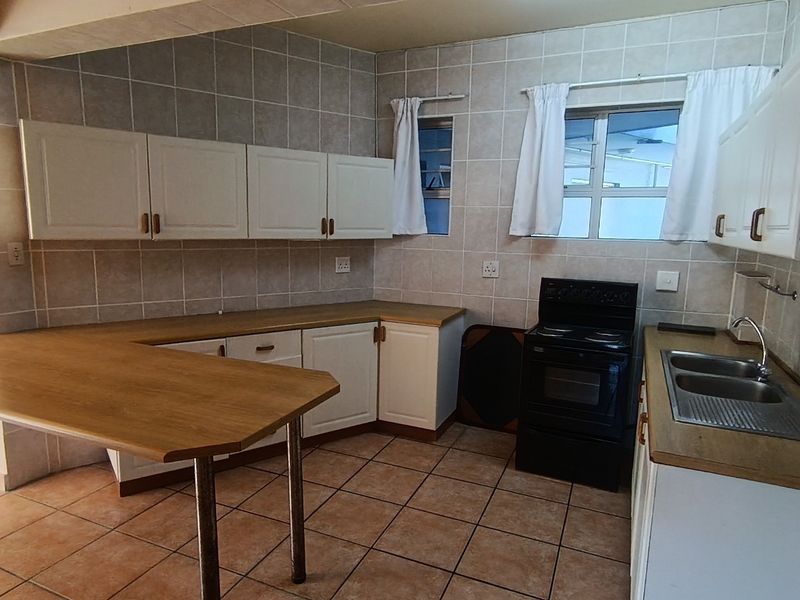 A functional kitchen featuring built-in cabinetry, laminate countertops, a double sink, and a breakfast nook, finished with ceramic wall and floor tiles.