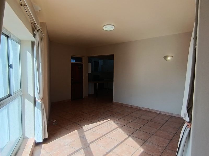 An empty, sunlit living area featuring tiled flooring and a sliding glass door leading to an outdoor space.
