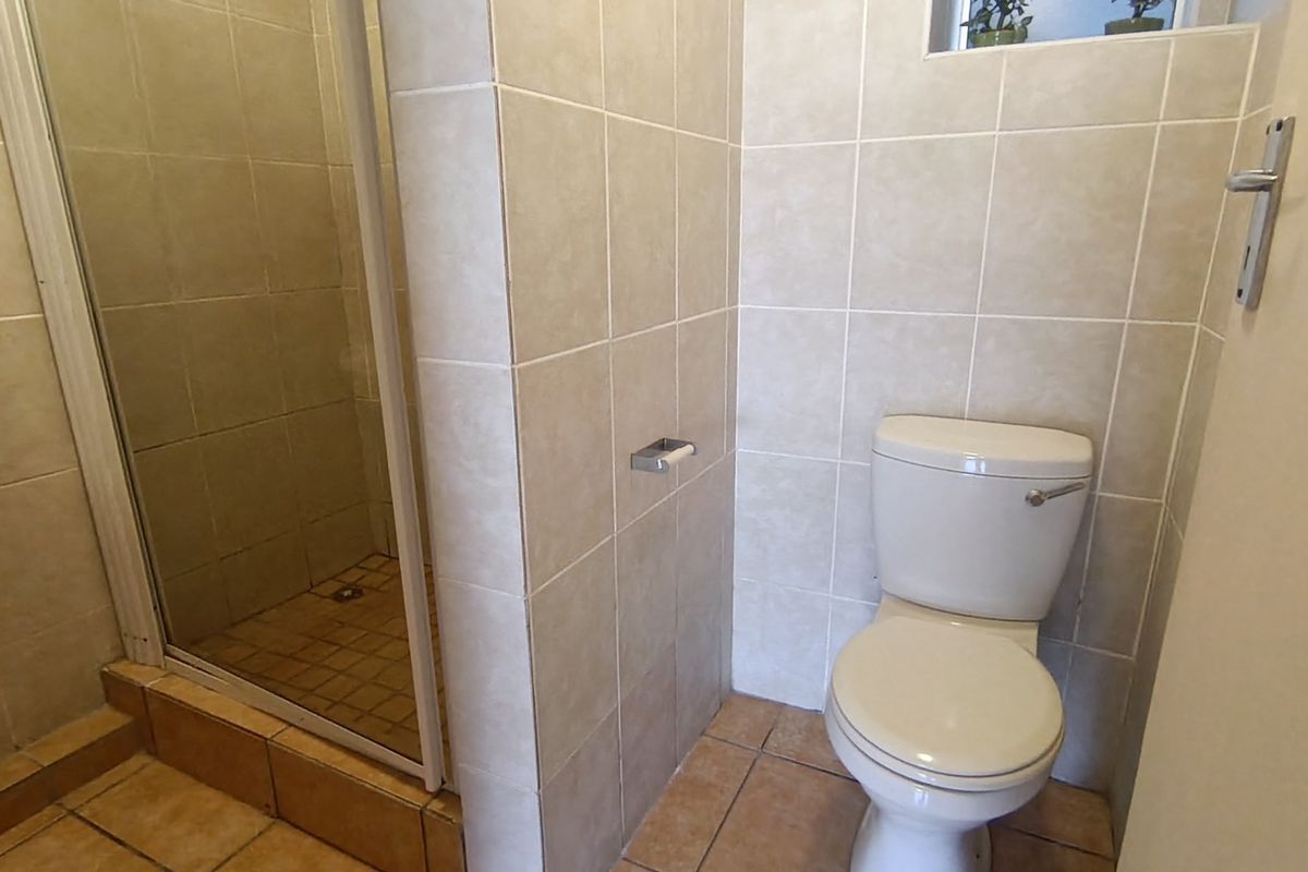A functional bathroom featuring a tiled shower enclosure and a standard toilet with neutral wall and floor tiling.
