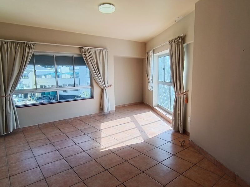A bright, empty living room featuring tiled flooring and large windows with natural light, offering a blank canvas for interior design.